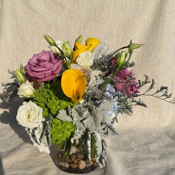 Mixed bouquet in a glass vase with yellow calla lilies, roses, and white blooms