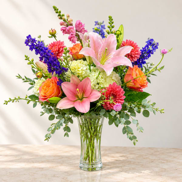 Mixed bouquet of pink lilies, roses, and purple flowers in a clear glass vase