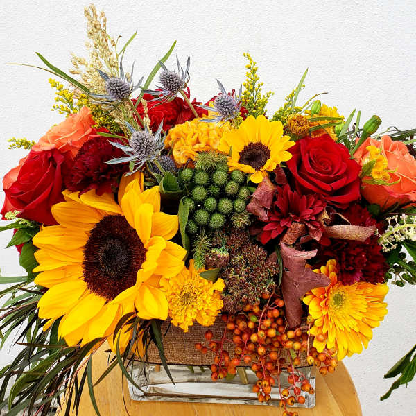 Bright mixed bouquet with sunflowers, roses, and orange blooms in a glass vase