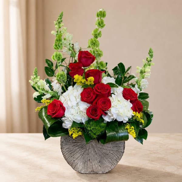 Red roses and white hydrangeas arranged in a gray vase with tall green spikes