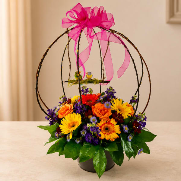 Colorful flower arrangement in a black container with a pink ribbon bow and bird cage topper