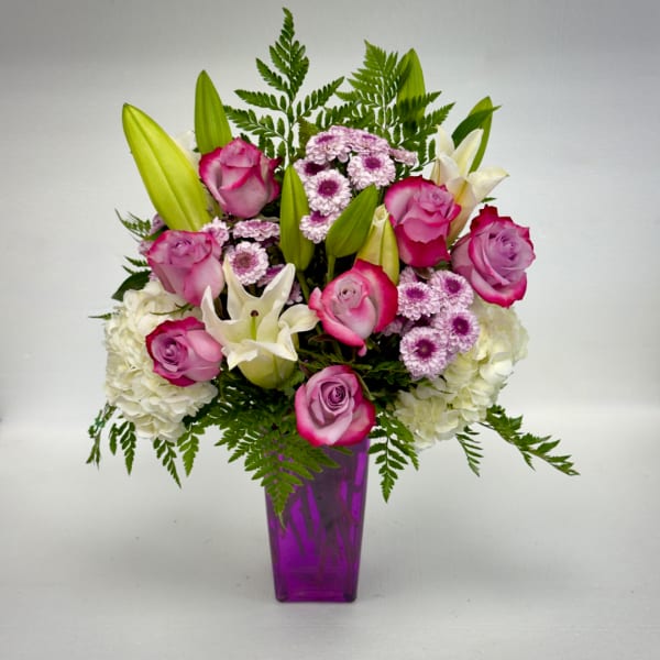 Pink roses and white lilies arranged in a purple vase