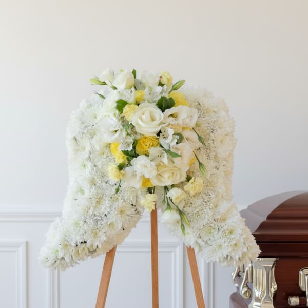 White floral funeral spray on a wooden easel beside a casket