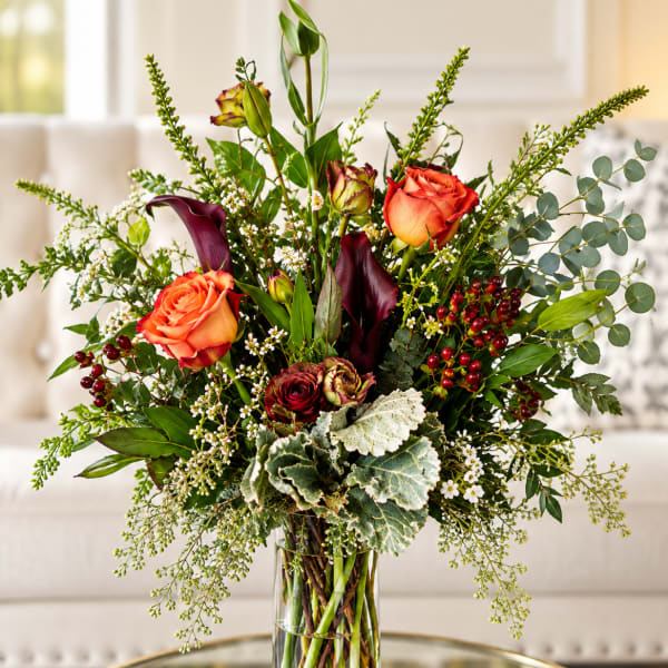 Tall bouquet of orange roses, dark calla lilies, and greenery in a glass vase