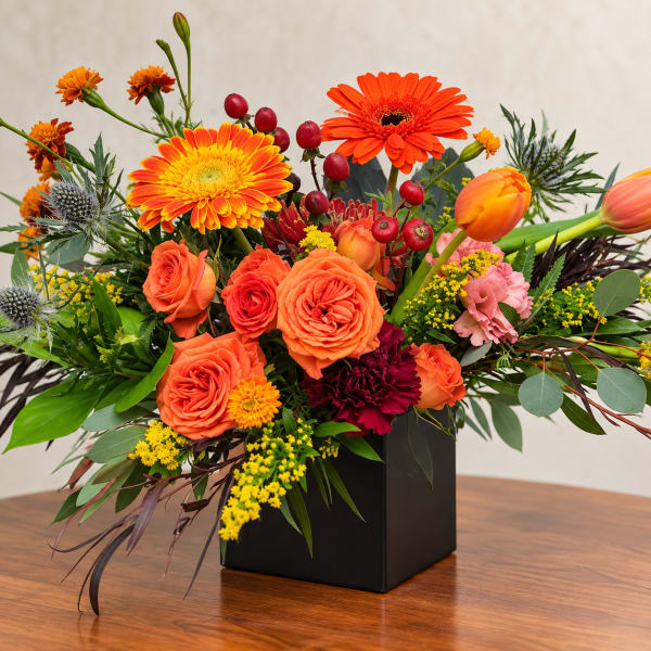 Orange and yellow mixed flower arrangement in a black square vase