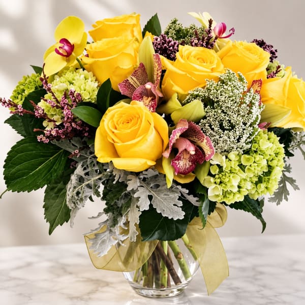 Yellow roses and orchids arranged in a clear glass vase
