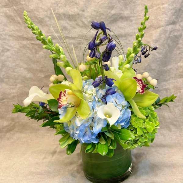 Blue hydrangeas with green orchids and white calla lilies in a green vase