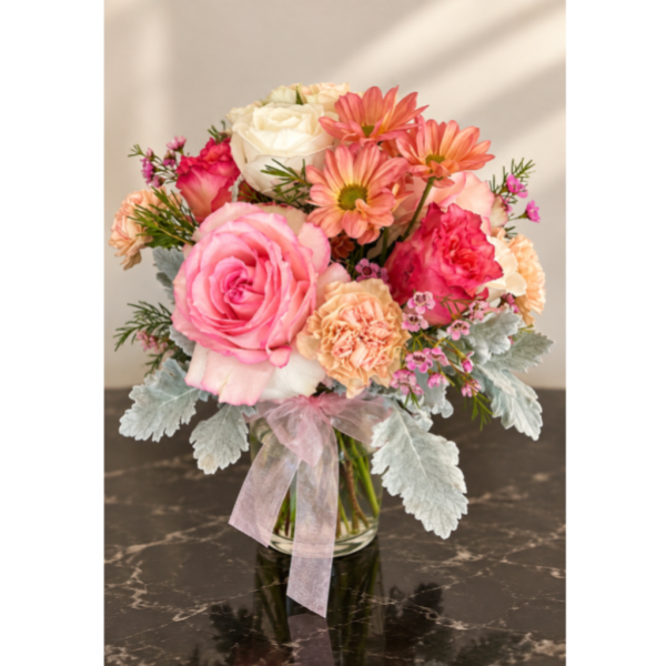 Pink and peach mixed flowers in a clear glass vase with a ribbon