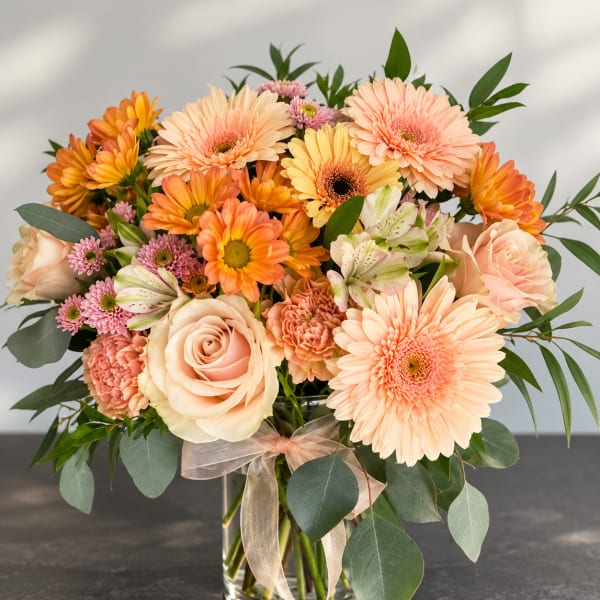 Peach and orange mixed bouquet in a clear glass vase with a ribbon