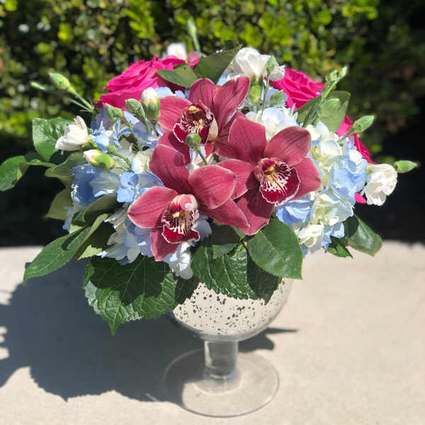 Pink orchids and blue hydrangeas in a glass goblet vase