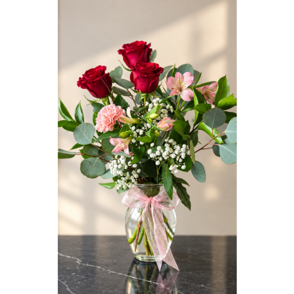Red roses and pink flowers in a glass vase with a pink ribbon