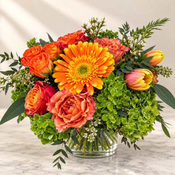 Bright mixed bouquet in a clear glass vase with orange roses and a yellow gerbera daisy
