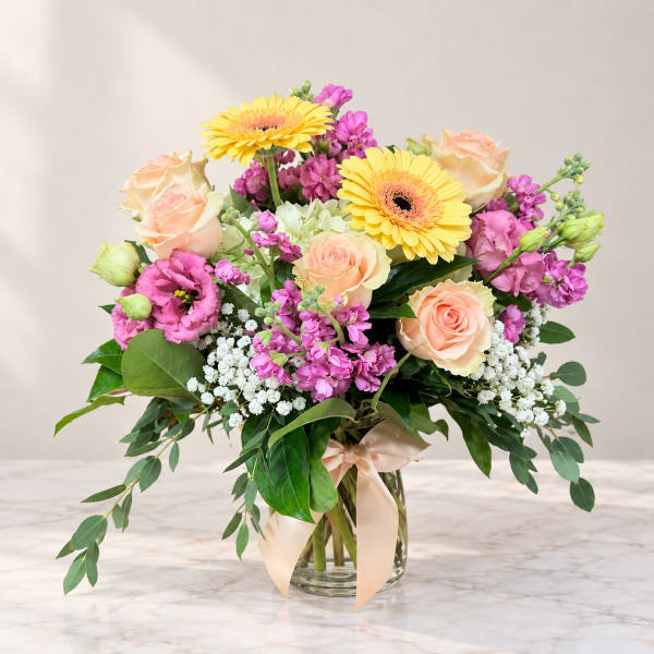 Bouquet of peach roses, yellow gerbera daisies, and pink flowers in a glass vase