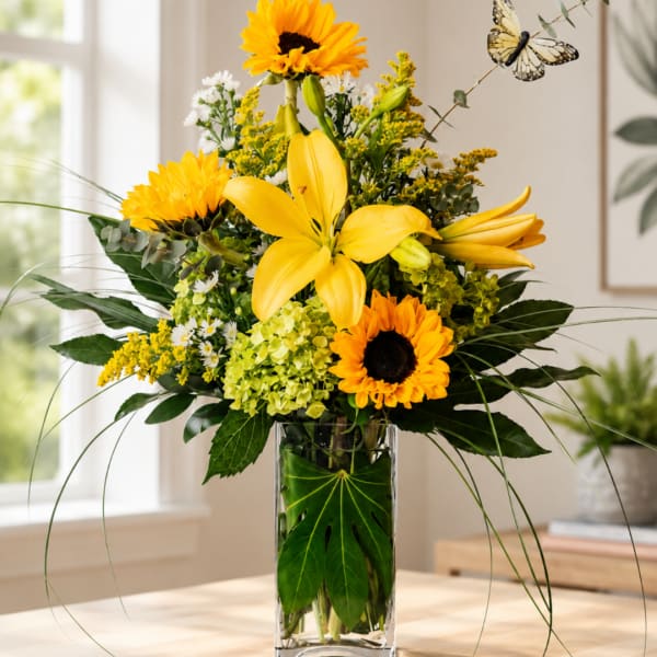Yellow lilies and sunflowers arranged in a clear glass vase