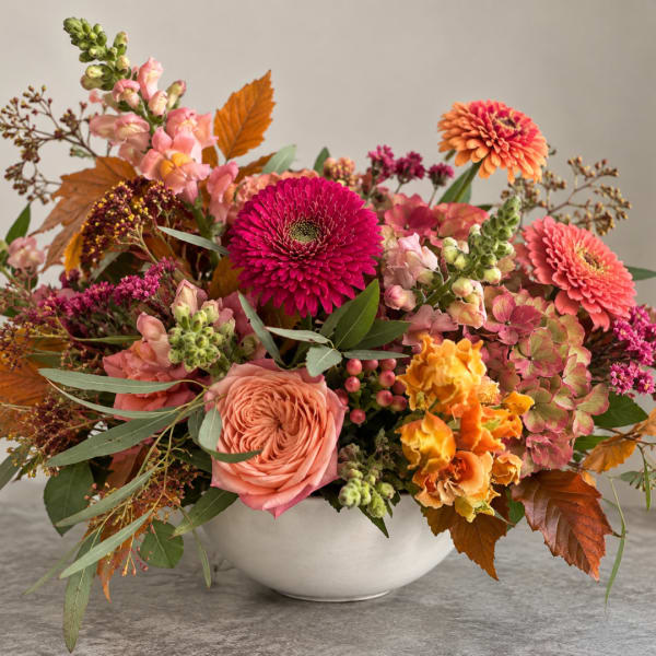 Mixed bouquet of pink, orange, and coral flowers in a white bowl vase