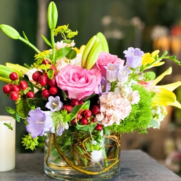 Pink roses and mixed blooms in a clear glass vase with red berries