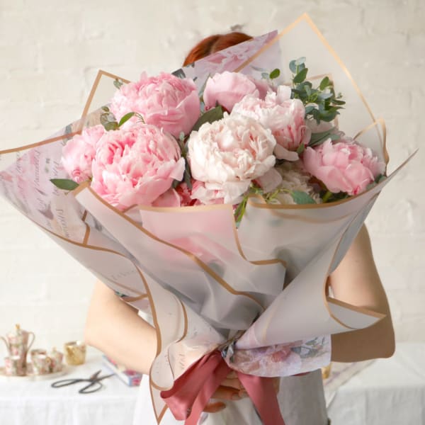 Pink peony bouquet wrapped in translucent paper with a ribbon