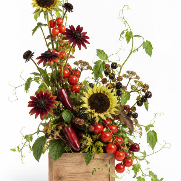 Mixed floral arrangement with sunflowers, dark daisies, berries, and tomatoes in a wooden box