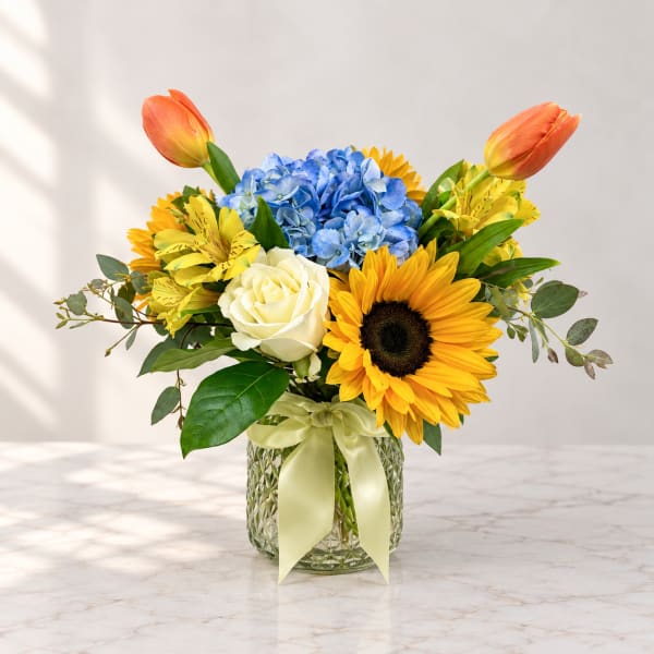 Bouquet of blue hydrangea, sunflowers, roses, and tulips in a glass vase