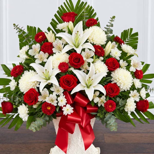 Large red, white, and green floral arrangement with lilies and roses in a white vase
