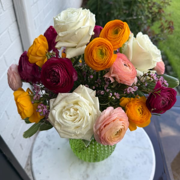 Mixed bouquet of roses and ranunculus in a green vase