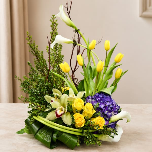 Yellow tulips, white calla lilies, purple hydrangea, and yellow roses in a low arrangement