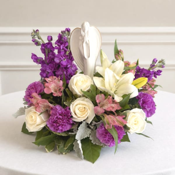 Purple and white floral arrangement with roses and lilies around a white angel figurine