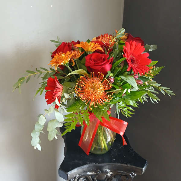 Red and orange mixed bouquet in a glass vase with a red ribbon