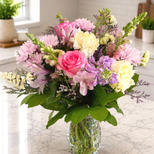 Mixed pink, purple, and cream flowers in a clear glass vase