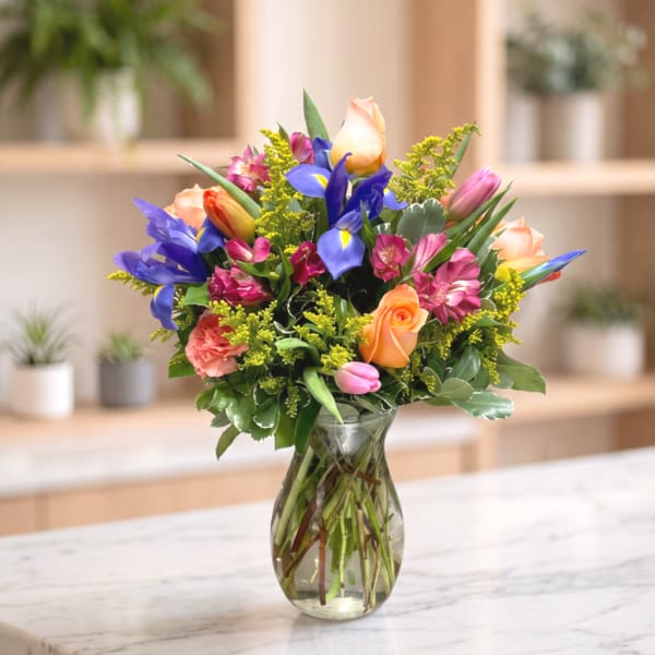 Mixed bouquet of roses, tulips, irises, and carnations in a clear glass vase