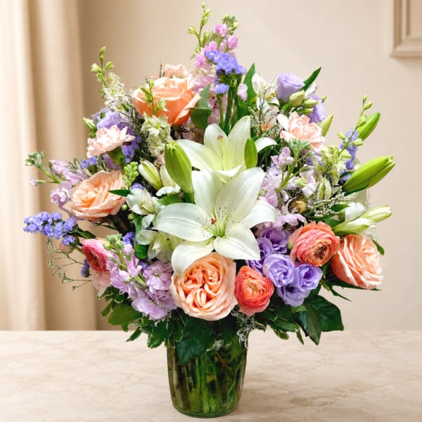 Mixed bouquet of lilies, roses, and purple blooms in a glass vase