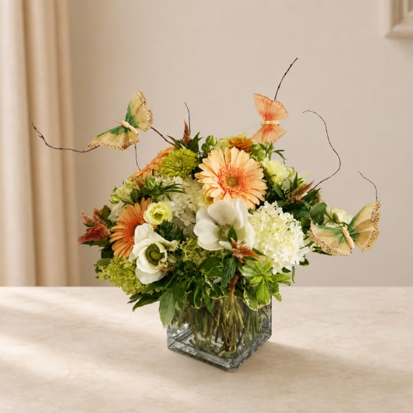 Mixed flower arrangement in a square glass vase with butterfly picks