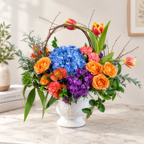 Colorful floral arrangement in a white pedestal vase with a twig arch