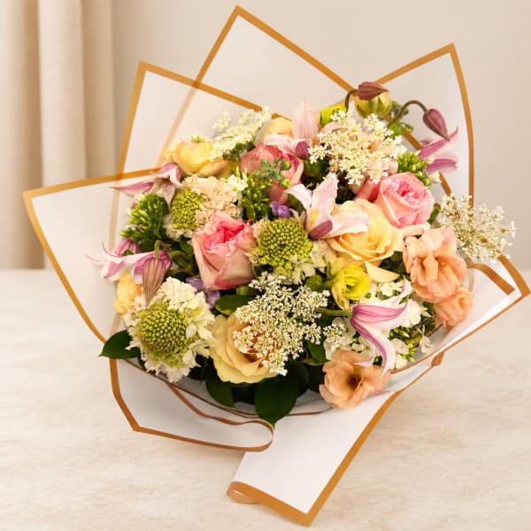Pastel bouquet of roses, lilies, and small white filler flowers wrapped in white paper