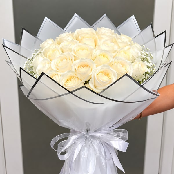 Bouquet of cream roses wrapped in white paper with a silver ribbon