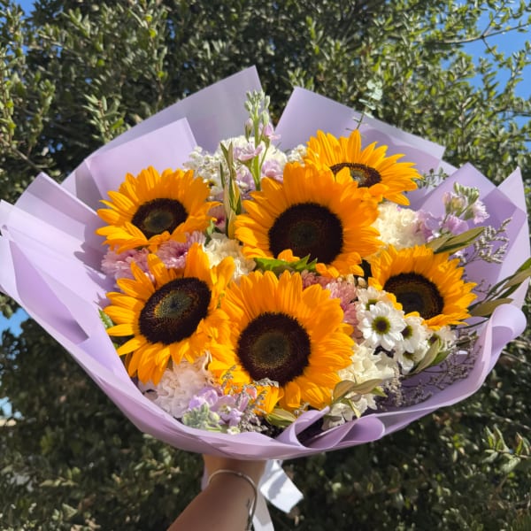 Bouquet of sunflowers and pastel flowers wrapped in lavender paper