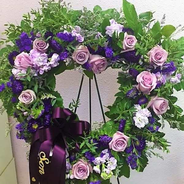 Purple and pink floral wreath on a stand with a ribbon bow