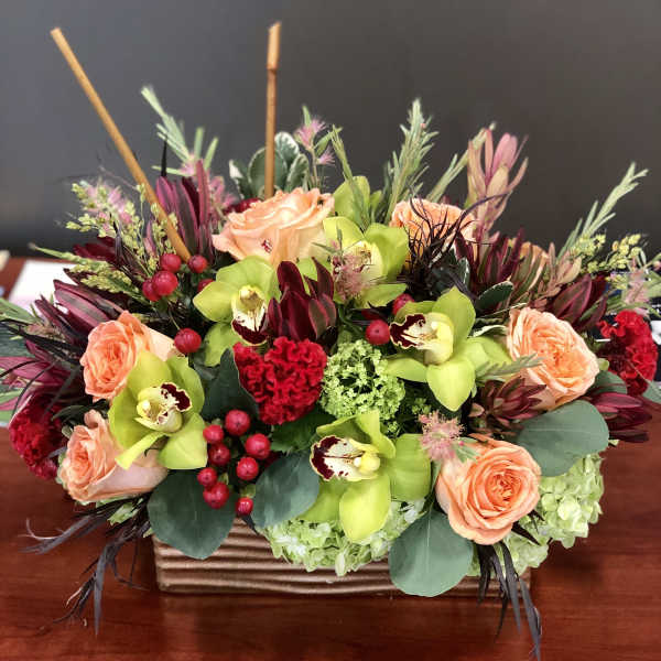 Peach roses and green orchids in a rectangular vase with red accents