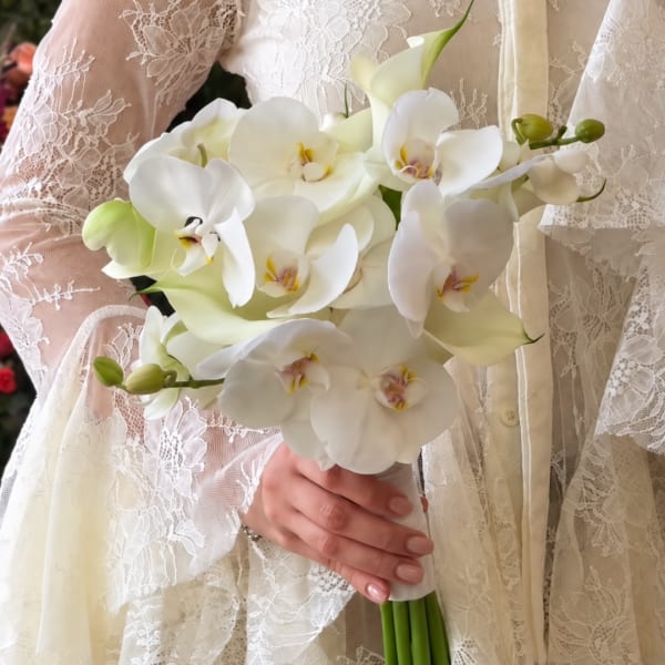 Bride holding a white orchid bouquet against a lace wedding dress