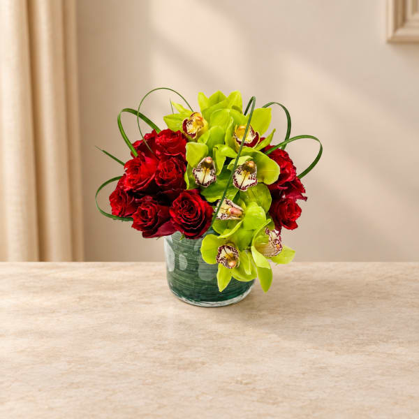 Red roses and lime green orchids arranged in a glass vase