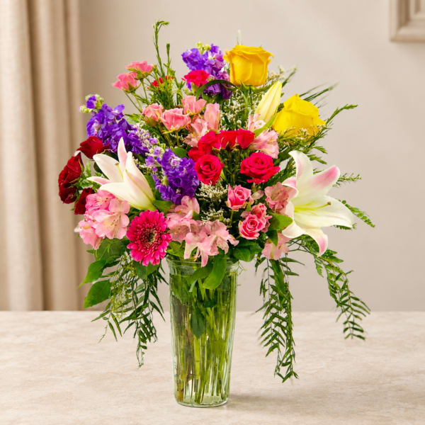 Mixed bouquet of roses, lilies, and pink and purple flowers in a glass vase