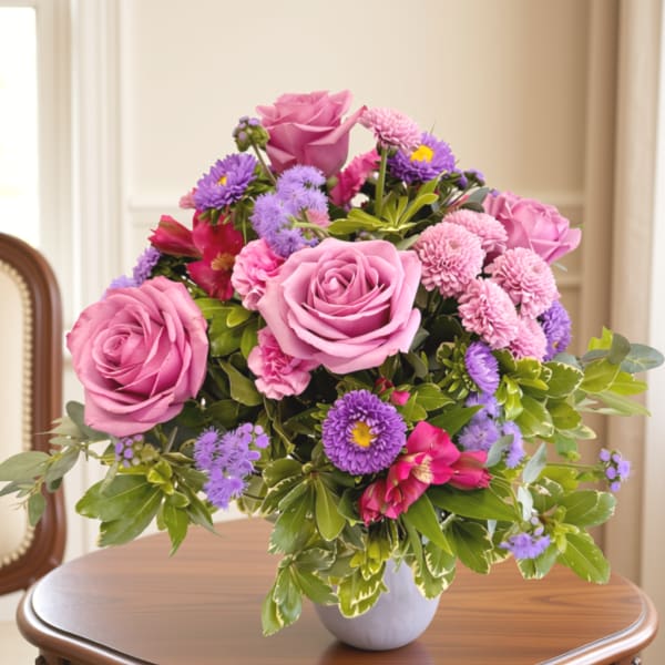 Pink roses and purple flowers arranged in a white vase