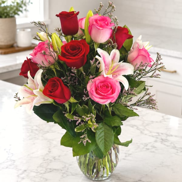Bouquet of red and pink roses with white lilies in a clear glass vase