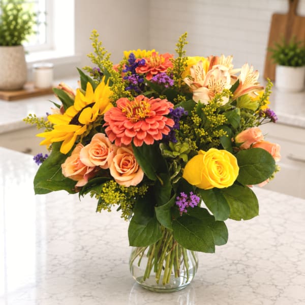 Mixed bouquet of sunflowers, roses, and alstroemeria in a clear glass vase