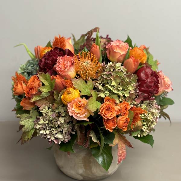 Low ceramic vase of orange and peach roses, hydrangeas, and mixed warm-toned flowers