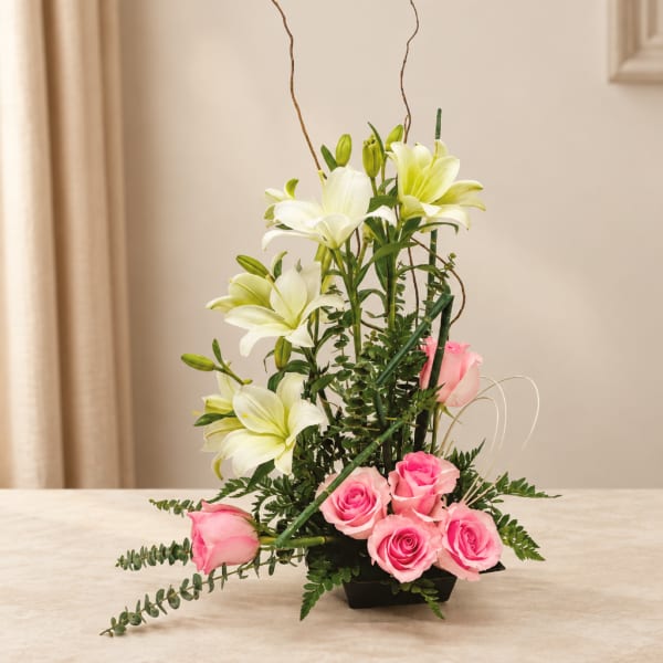 Pink roses and white lilies arranged in a black vase with curly branches