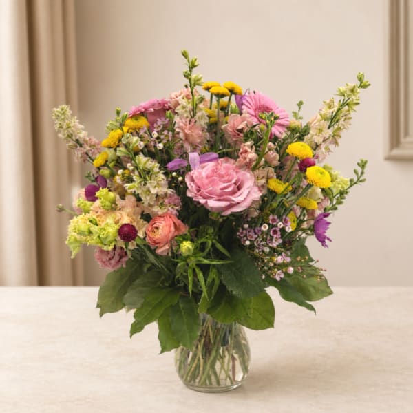 Mixed pink, yellow, and purple flowers arranged in a clear glass vase.