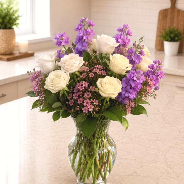 White roses and purple flowers arranged in a clear glass vase