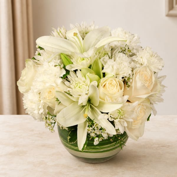 White lilies, roses, and mums arranged in a green glass vase