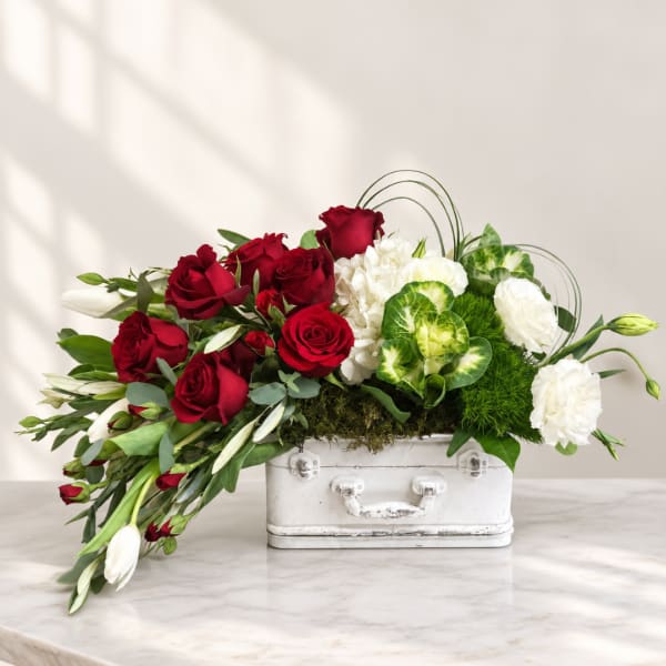 Red roses and white flowers arranged in a white suitcase-style container